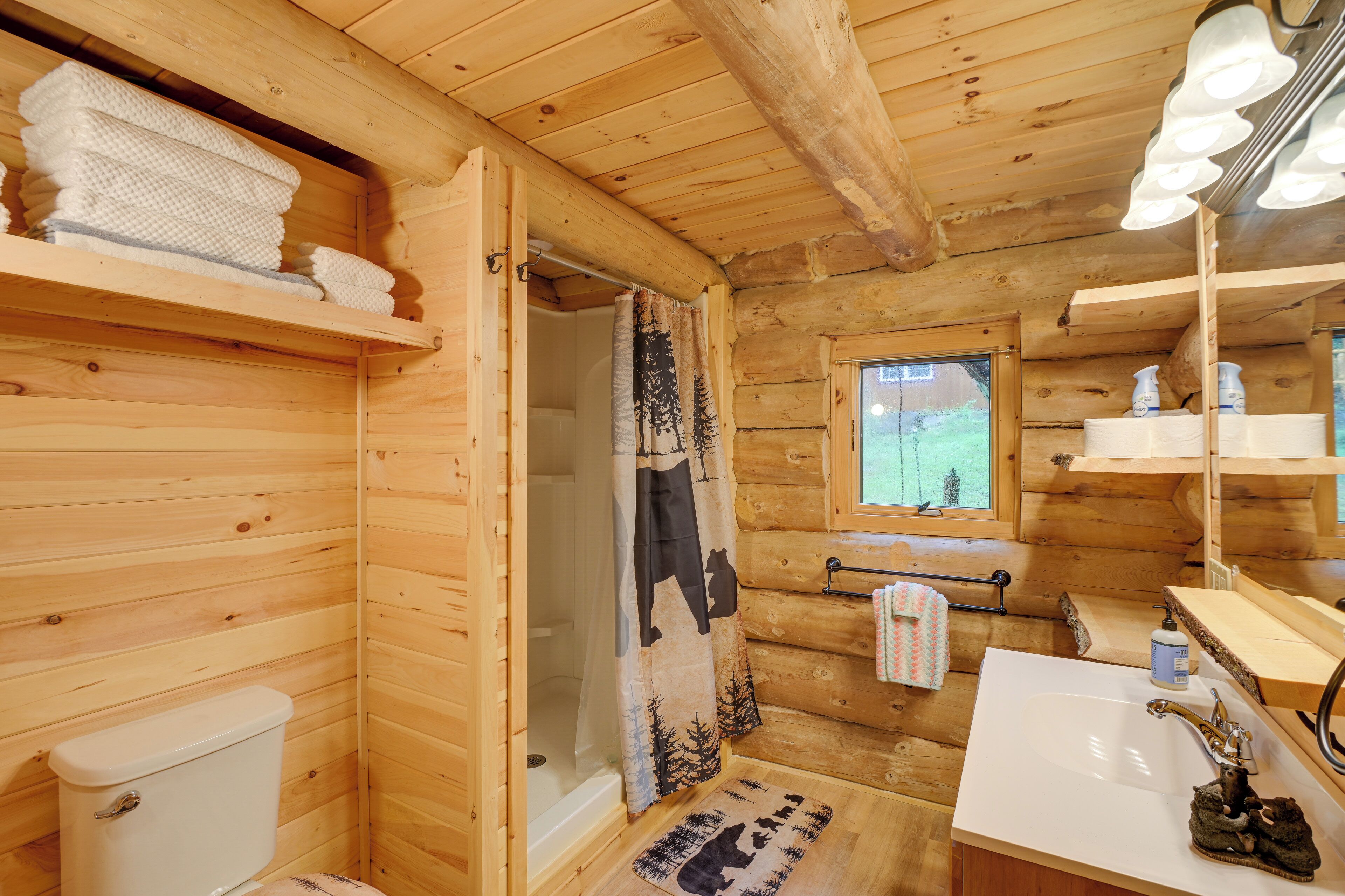 Une salle de bain rustique, aménagée dans une cabane en bois, comprenant des toilettes, une douche, un lavabo et une fenêtre.