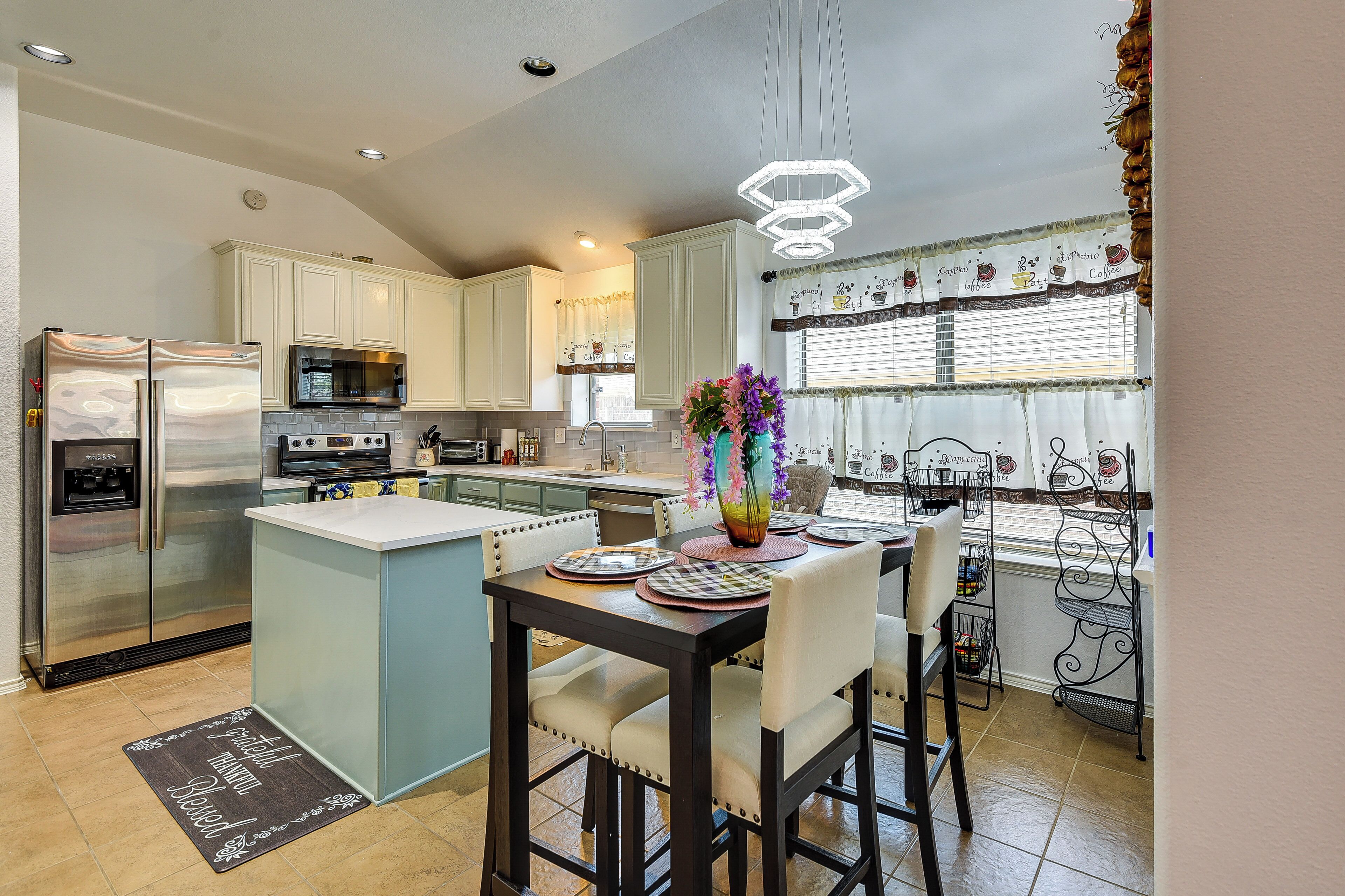 A kitchen with white cabinets, a stainless steel refrigerator, a microwave, and a dining area with a table set for two.