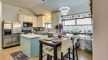 A kitchen with white cabinets, a stainless steel refrigerator, a microwave, and a dining area with a table set for two.