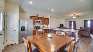 A modern kitchen with wooden cabinets, a stainless steel refrigerator, and a dining area with a wooden table and chairs. - Charming Arkansas Getaway - Walk to Downtown! (Fort Smith)