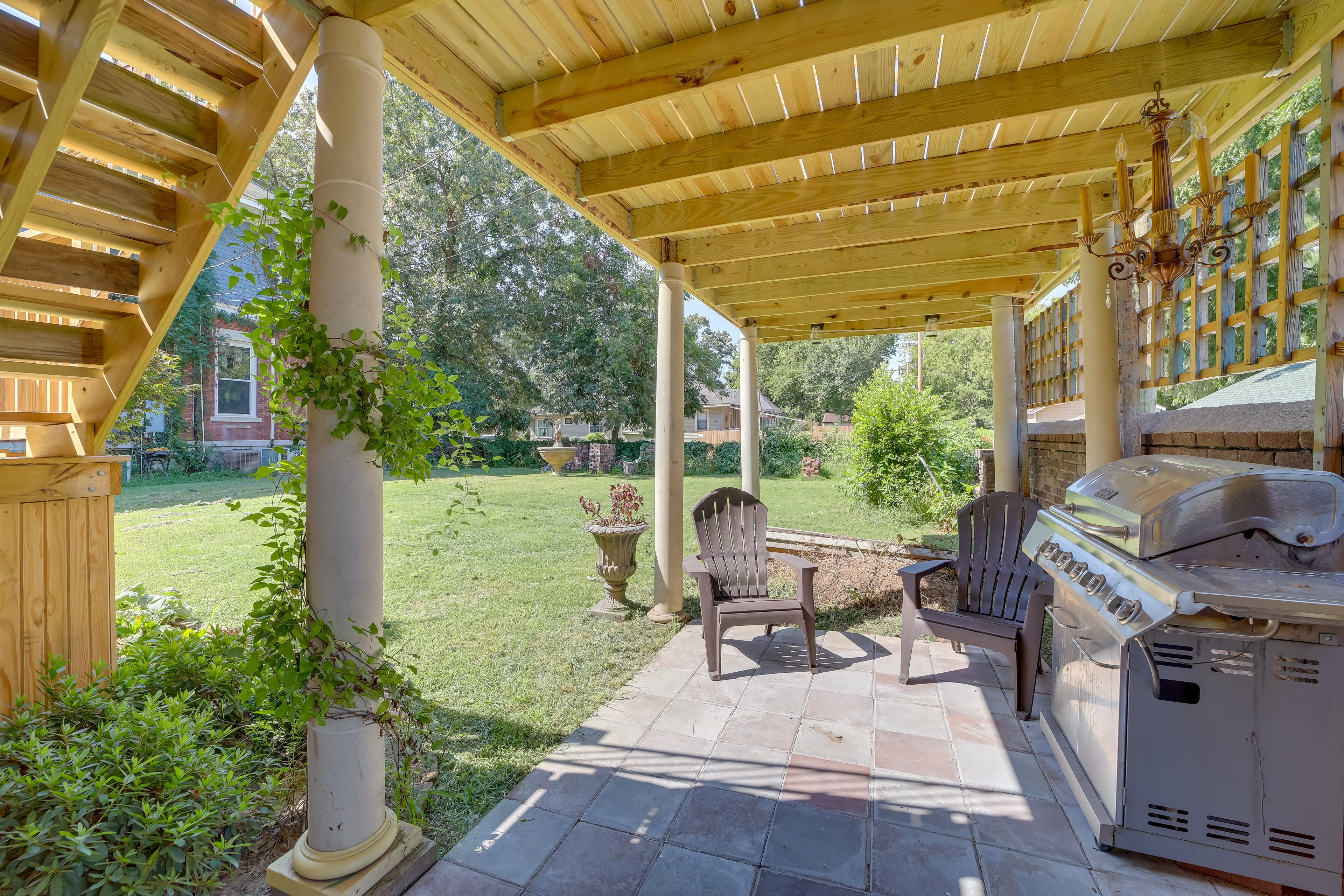 A covered patio with a grill, seating, and a view of the backyard.