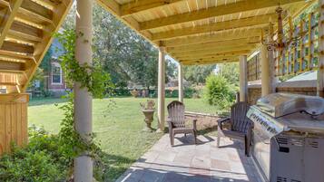 A covered patio with a grill, seating, and a view of the backyard.