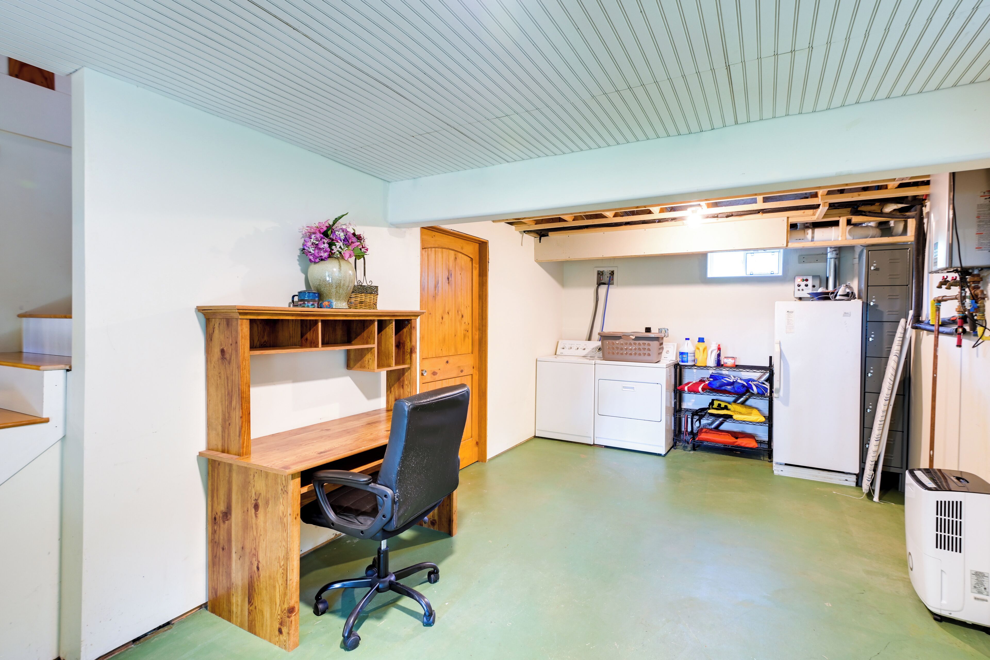 Una cocina compacta con un escritorio de madera, una silla y un estante pequeño con un jarrón.