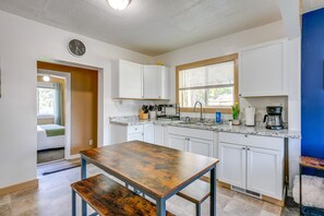 Una cocina moderna con armarios blancos, una mesa de madera y una ventana con persianas.