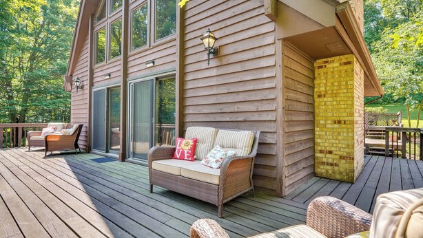 A wooden deck with wicker furniture, a glass door entrance, and a brick wall. - Cabin w/ Deck ~ 3 Mi to Apple Valley Lake! (Howard)
