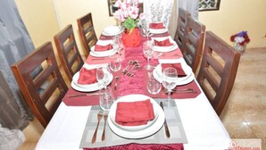 Mesa de comedor preparada para seis personas, con servilletas rojas, platos blancos y cubiertos.