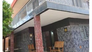 Una casa de dos pisos con balcón, un porche con tejas y un muro de piedra.