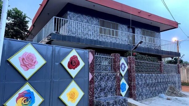 Una casa de dos pisos con un balcón, una valla decorativa con paneles en forma de rombo y un muro de piedra.