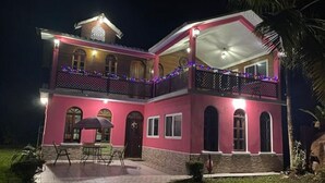 Une maison à deux étages dotée d’un balcon, d’une terrasse couverte et d’un petit jardin.