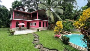 Une maison à deux étages dotée d’un balcon, entourée d’une pelouse bien entretenue et d’une piscine.