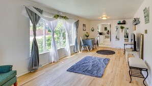 A room with a wooden floor, a blue rug, a green sofa, a dining table with chairs, a kitchen area, and a small bench. - Gillette Adventure Base 1 Mi to Historic Downtown! (Gillette)