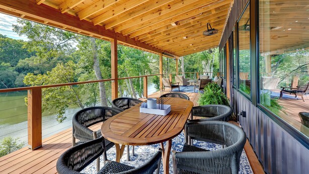 Eine Holzterrasse mit Tisch und Stühlen, mit Blick auf einen See, umgeben von Bäumen.