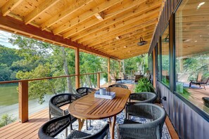 A wooden deck with a table and chairs, overlooking a lake and surrounded by trees. - Modern, Riverfront Family House w/ Balcony & Grill (Arkadelphia)