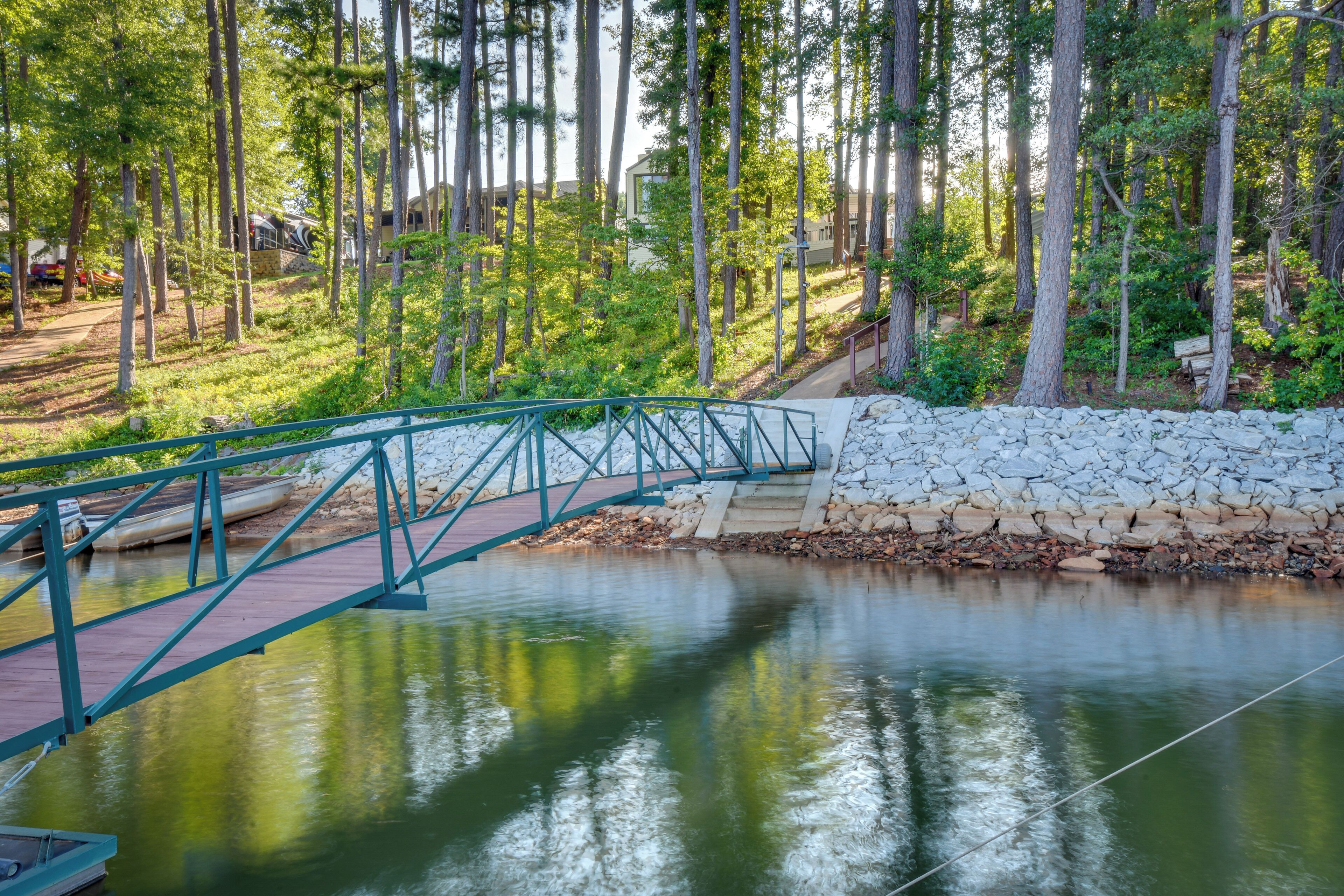 Un pont en bois enjambant une rivière paisible, entouré d’arbres et d’un mur de pierre.