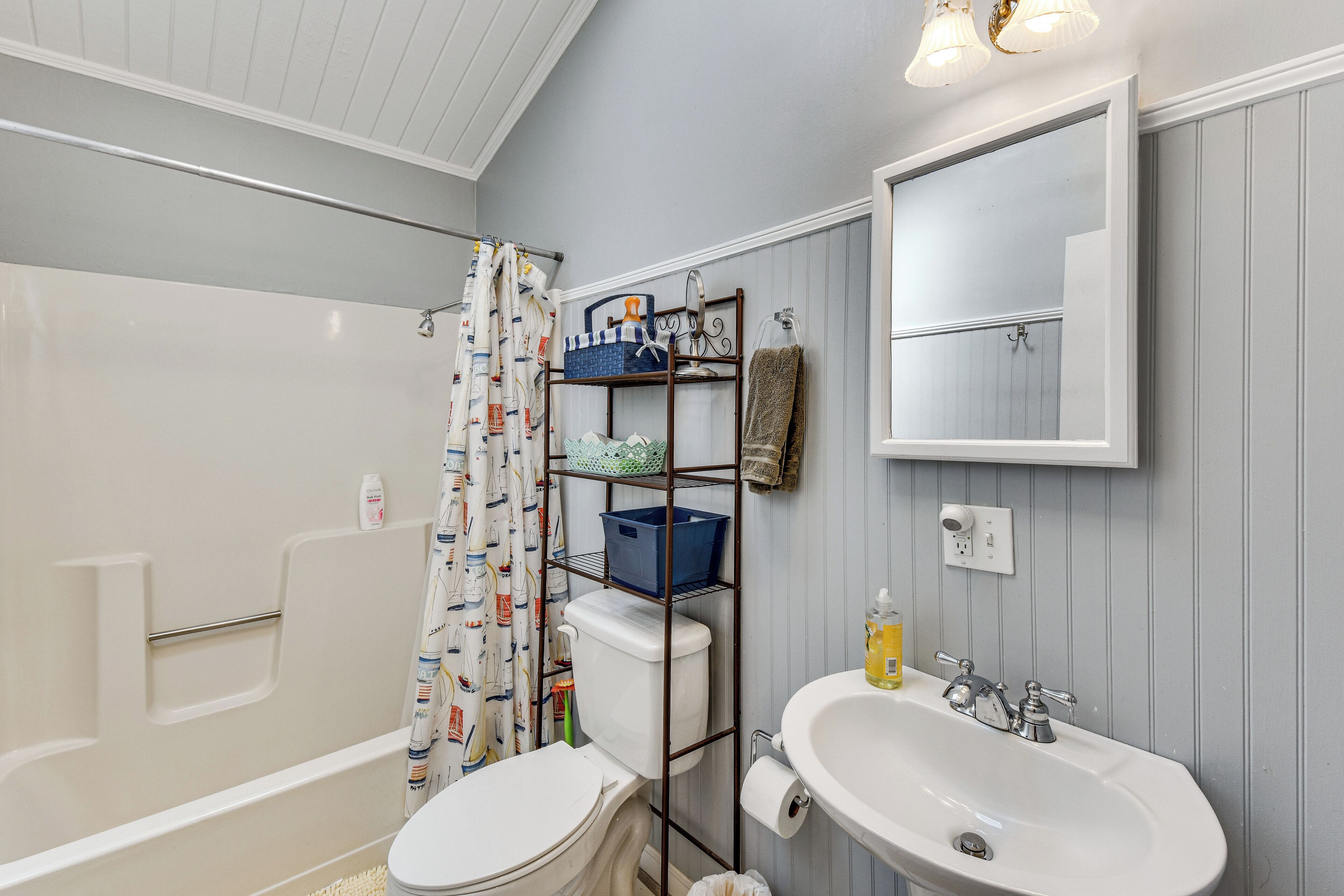 A bathroom with a bathtub, toilet, sink, and shelves with toiletries.
