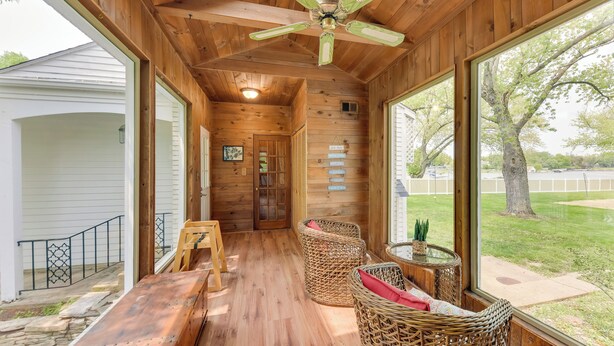 A wooden interior with a ceiling fan, wicker chairs, a wooden table, and large windows offering a view of the outdoors. - Pistakee Lake Estate w/ Boat Dock & Hot Tub! (McHenry)