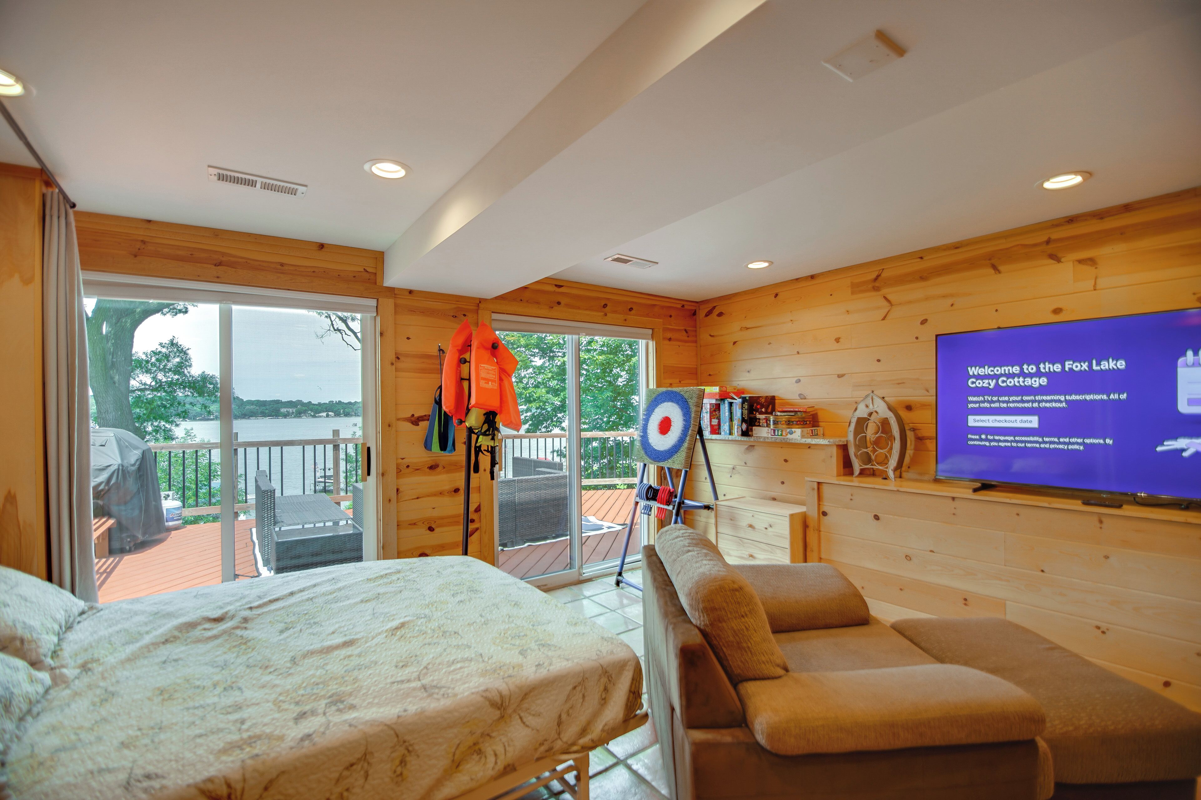 A cozy cabin with a bed, a sofa, a TV, and a balcony with a view of the lake.