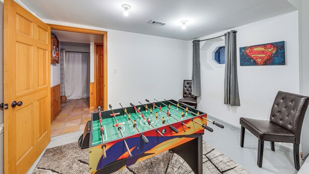 A room with a foosball table, a chair, a Superman painting, and a door leading to another room.