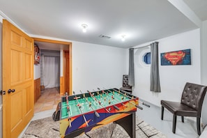 A room with a foosball table, a chair, a Superman painting, and a door leading to another room. - Waterfront Fox Lake Vacation Rental w/ Fire Pit! (Fox Lake)