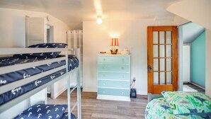 Ein Zimmer mit Etagenbetten, einem Schminktisch, einer Lampe und einer Tür zu einem anderen Raum.