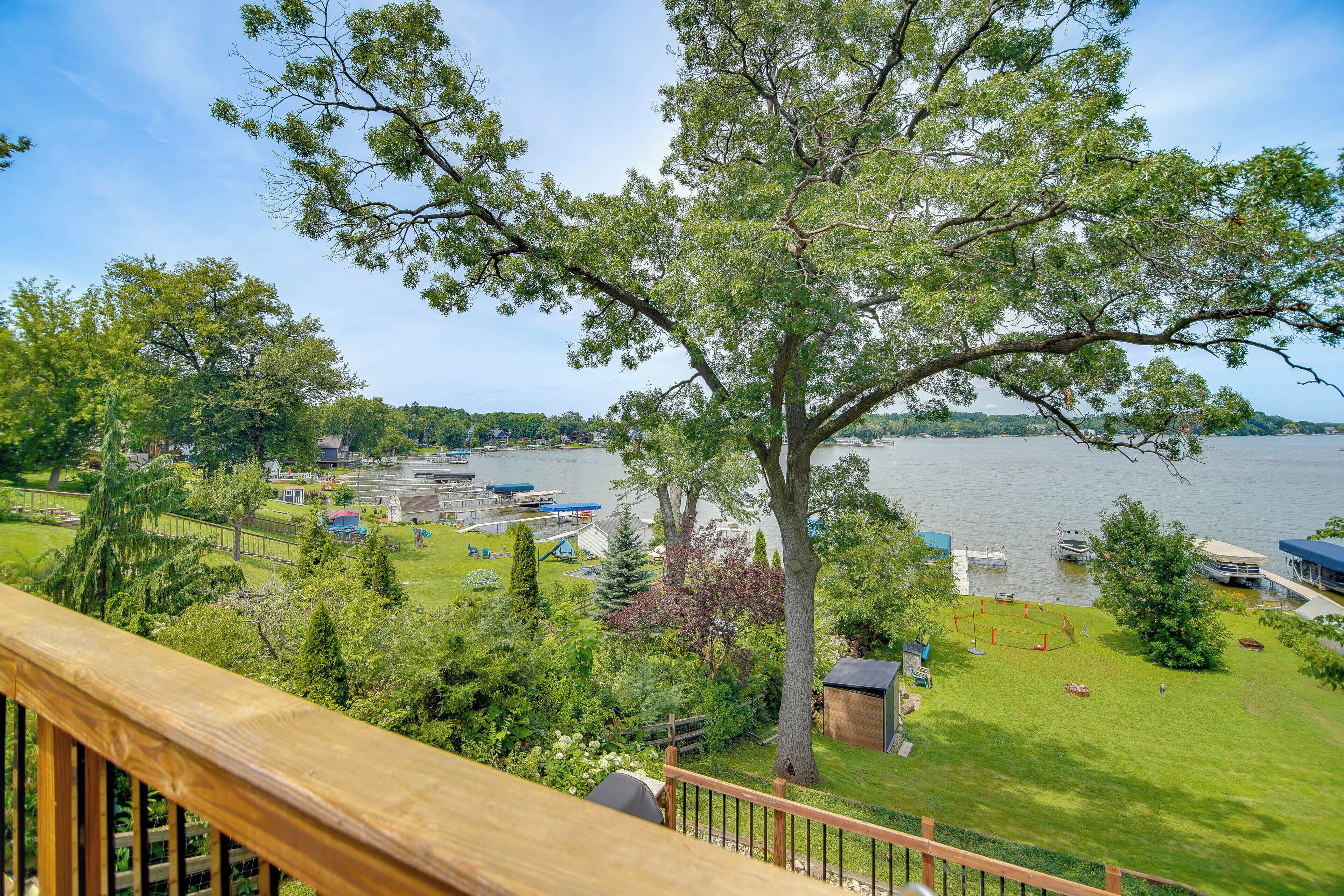 A lakeside property with a large tree, grassy areas, and boats docked.