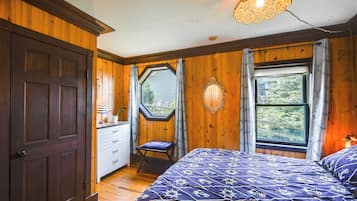 A bedroom with a large bed, a window with a view, a door, and a small table with a lamp.