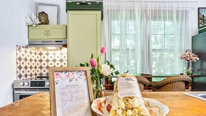 Et køkken med et træbord, et velkomstskilt i ramme, en skål med popcorn og en vase med blomster.
