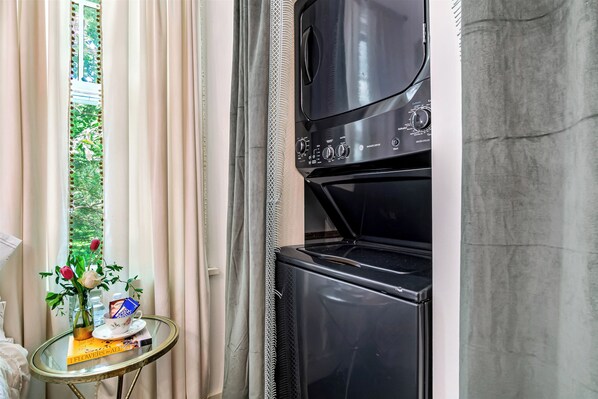 A room with a black oven, a glass table with a book and a cup, and a window with curtains.