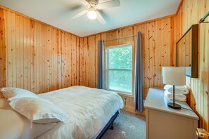 A bedroom with a bed, a nightstand, a lamp, a window, and a ceiling fan. - Lakefront Grant Cottage w/ Grill & Fire Pit! (Grant)