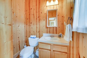 A wooden-paneled bathroom with a toilet, sink, mirror, and towel rack. - Lakefront Grant Cottage w/ Grill & Fire Pit! (Grant)