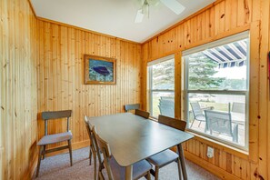 A wooden-paneled room with a table and chairs, a ceiling fan, and a window with a view of the outdoors. - Lakefront Grant Cottage w/ Grill & Fire Pit! (Grant)