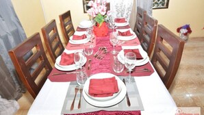 Une table à manger dressée pour six personnes, avec des serviettes rouges, des assiettes blanches et des couverts en argent.
