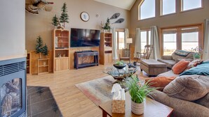 A spacious living room with a fireplace, a large flat-screen TV, wooden shelving, a glass coffee table, and a comfortable seating area with a sofa and armchairs. - Lakefront Grand Rapids Vacation Rental w/ Dock! (Grand Rapids)