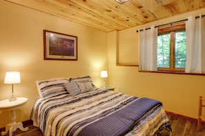 Um quarto com uma cama, duas luminárias de cabeceira, um quadro na parede e uma janela com cortinas.