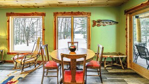 A dining area with a wooden table and chairs, large windows with a view of trees, and a fish decoration on the wall. - Pokegama Lake Vacation Rental w/ Shared Boat Dock! (Grand Rapids)