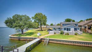 A lakeside property with a dock, a house with a covered patio, and a grassy area with trees. - Cedar Creek Lake Views: Gorgeous Mabank House! (Mabank)