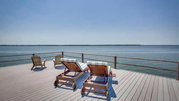 A wooden deck with lounge chairs and a table, overlooking a calm body of water. - Cedar Creek Lake Views: Gorgeous Mabank House! (Mabank)
