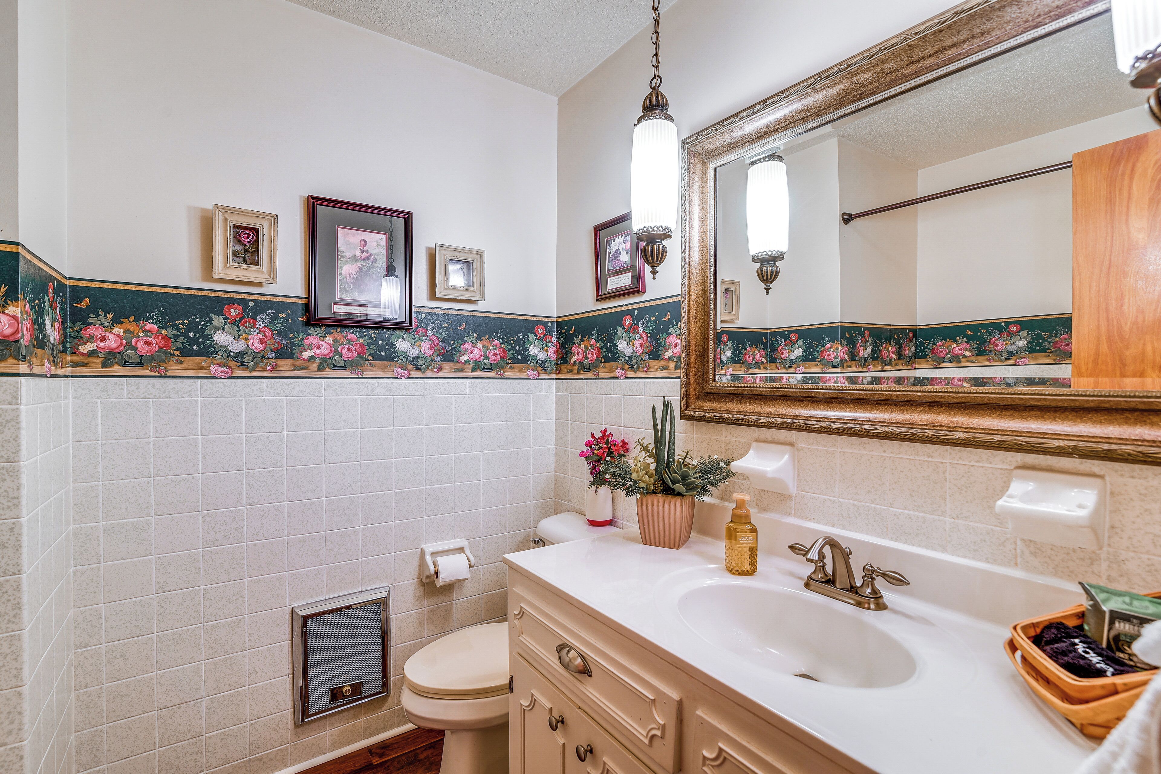 A bathroom with a white sink, a mirror, and a toilet. There are framed pictures on the wall and a floral border.