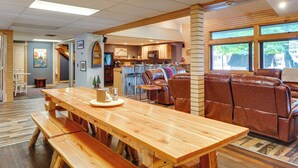 A spacious living area with a wooden dining table, leather sofa, and a kitchen in the background. - Spacious Old Forge Condo w/ Patio & Fire Pit! (Old Forge)