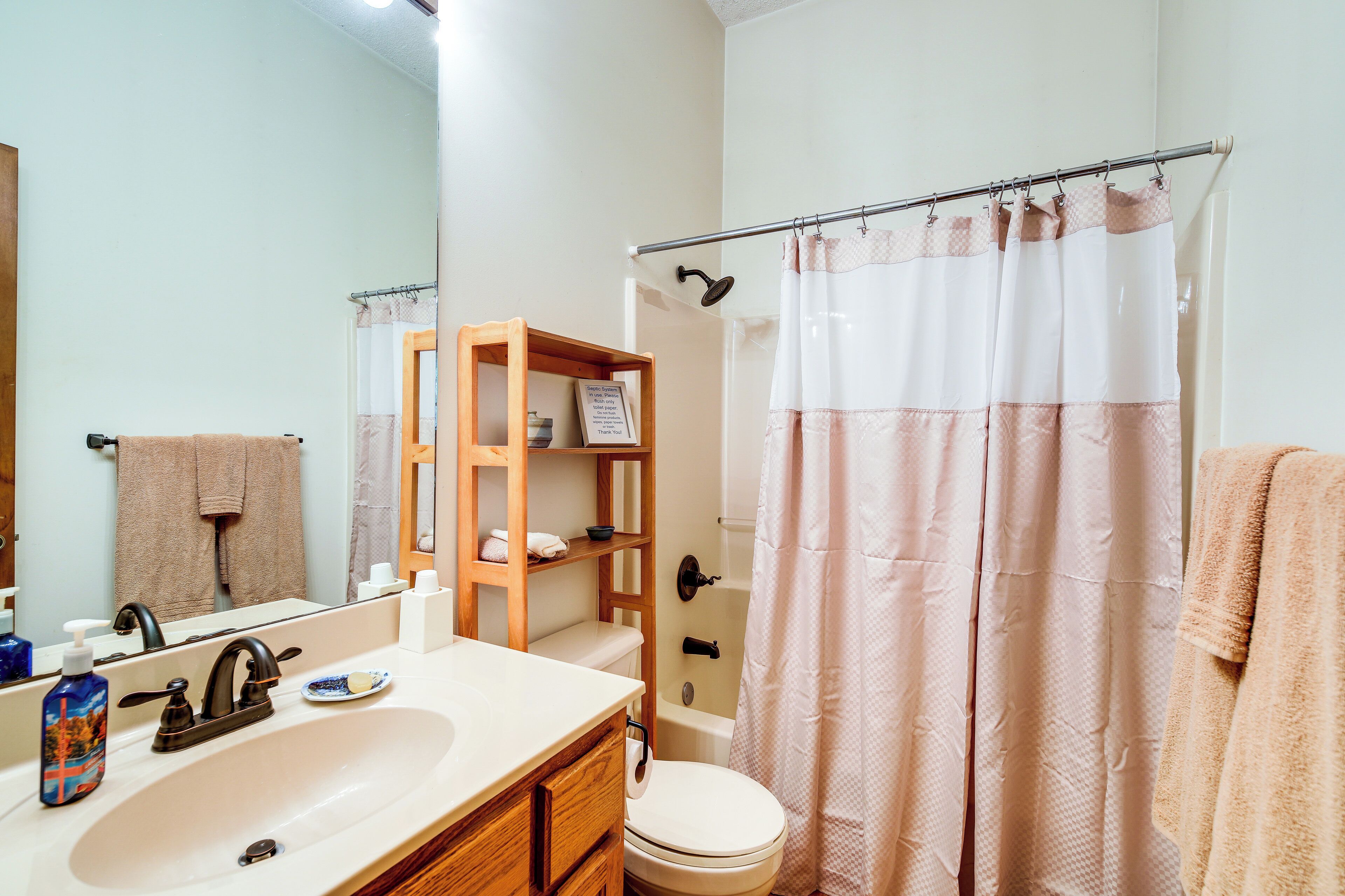 A bathroom with a sink, mirror, toilet, shower curtain, and wooden shelves.