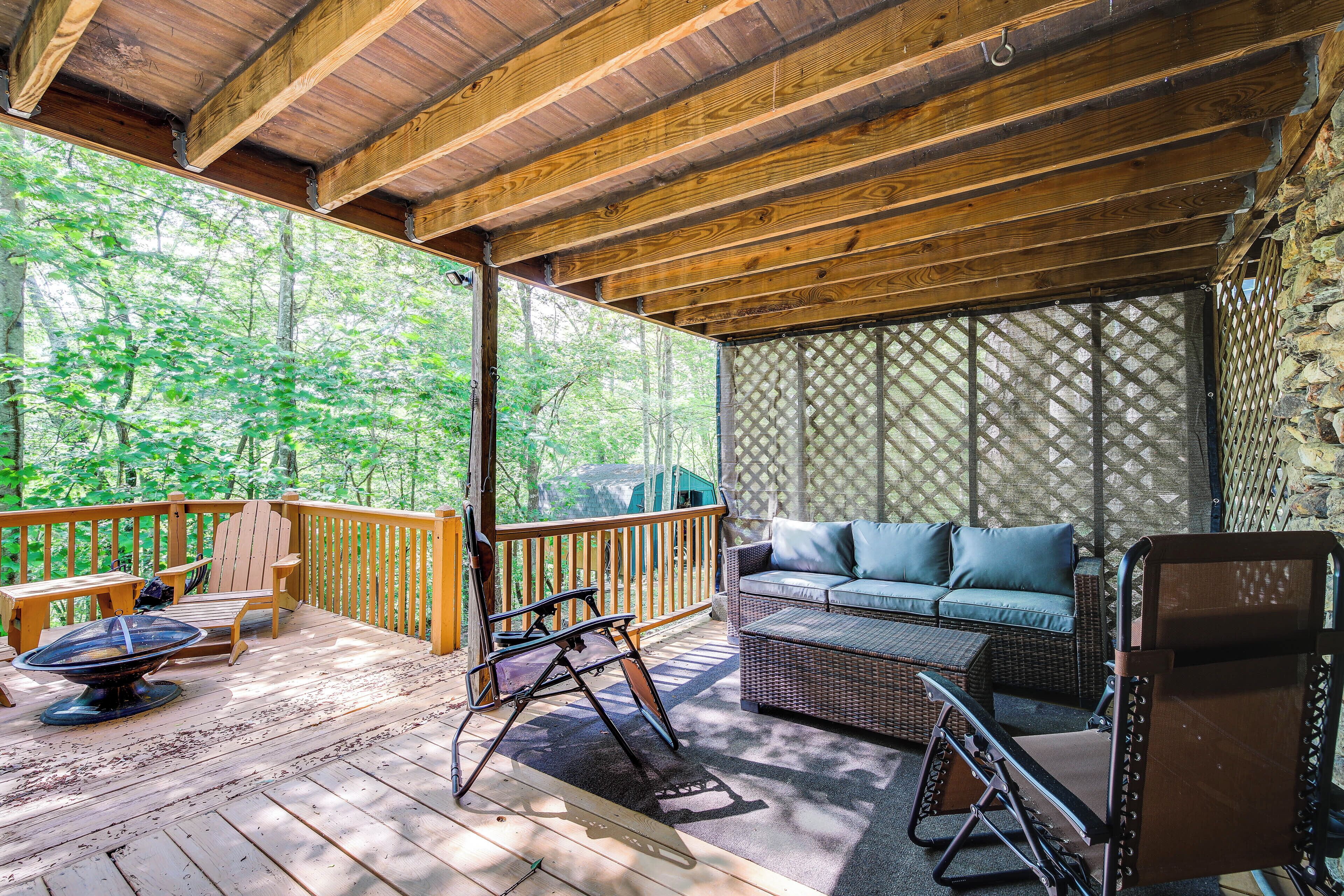 A wooden deck with outdoor furniture, including a sofa and chairs, overlooking a forested area.