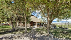 A rustic lodge with a stone exterior, a gravel driveway, and a swing set in the yard. - Scenic Mount Sopris View: Historic Alpine Cabin! (Glenwood Springs)