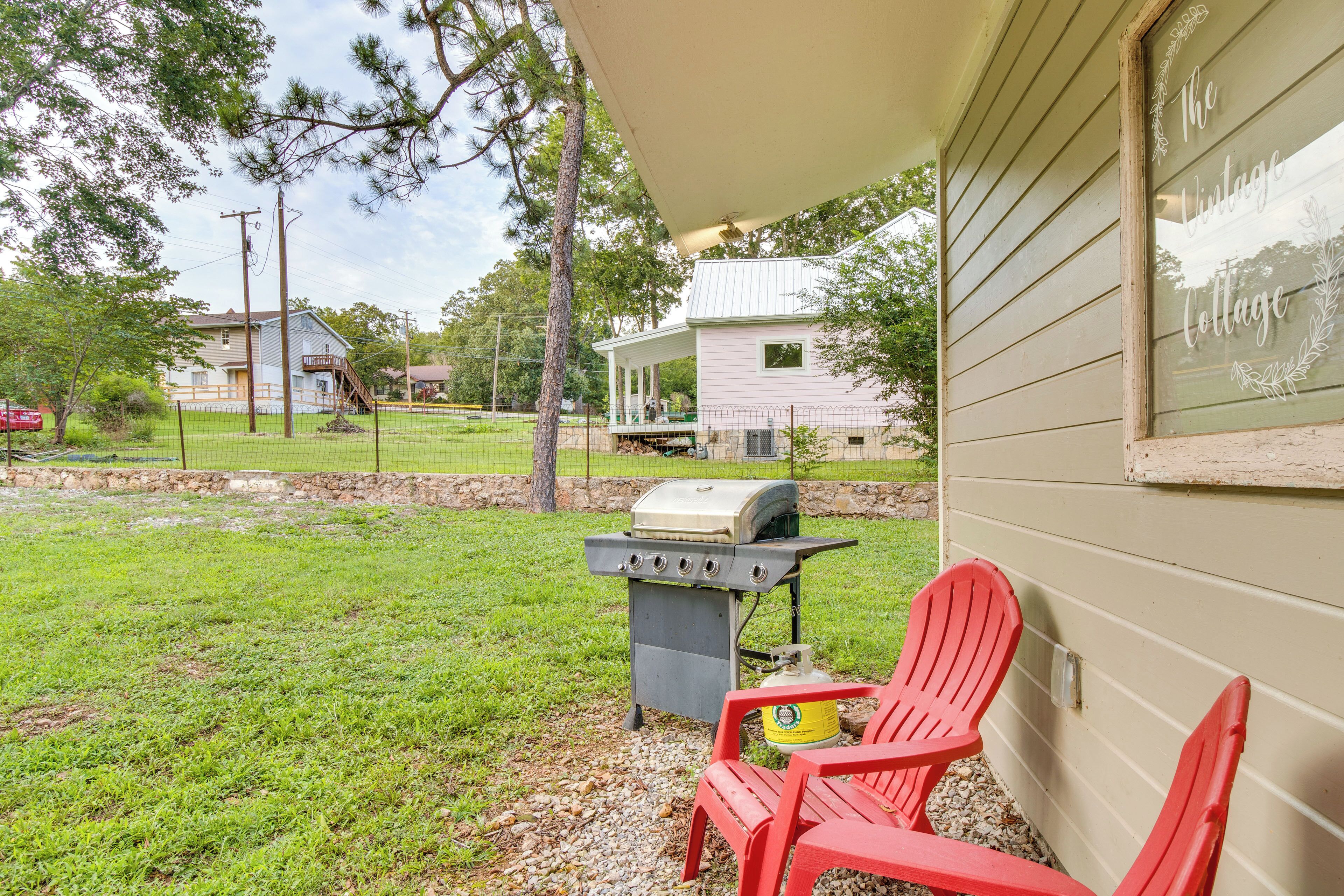 A backyard with a grill, a red chair, and a house in the background.
