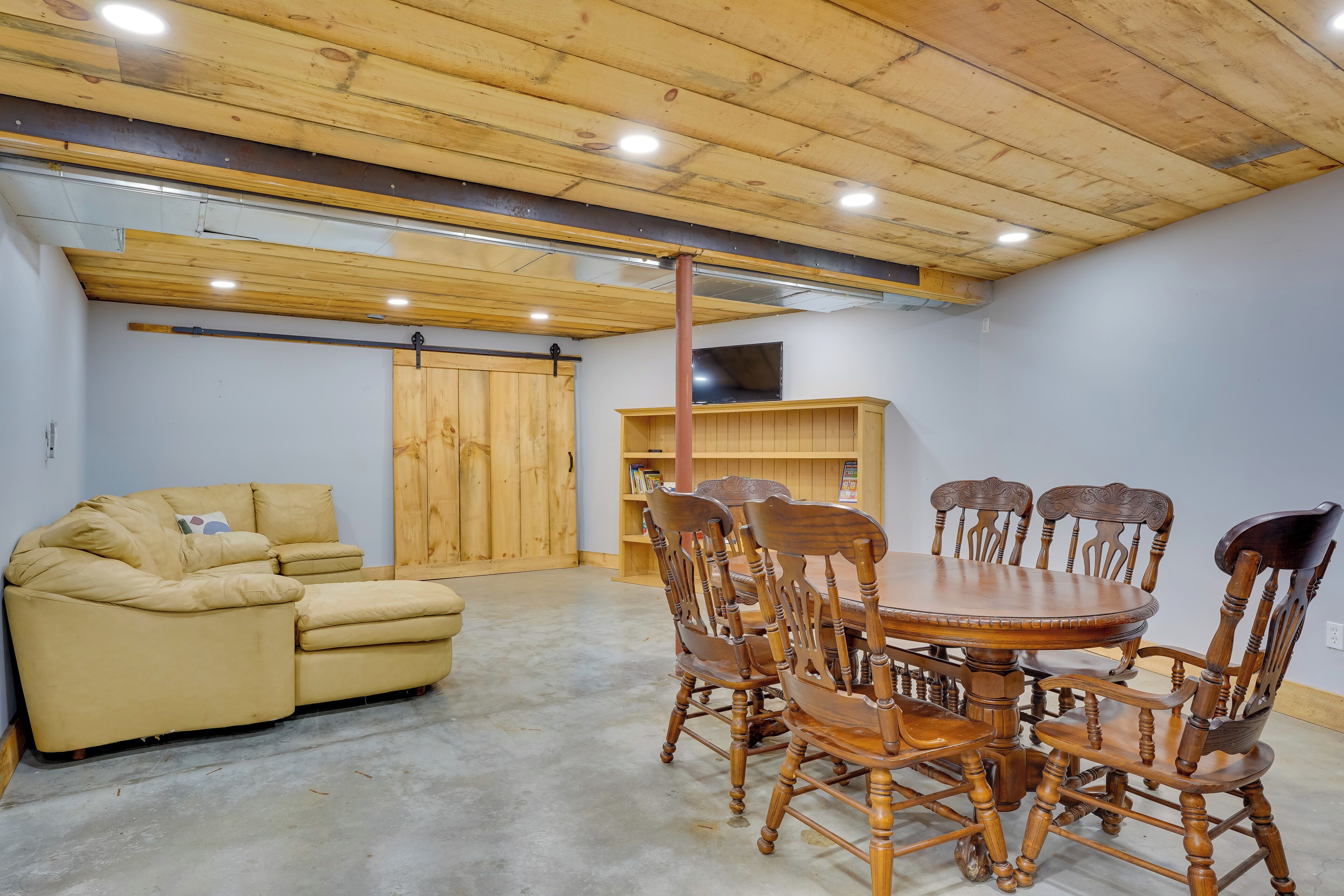 Una habitación con techo de madera, un sofá color beige, una mesa de comedor de madera con sillas y una estantería.