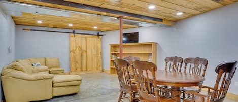 Una habitación con techo de madera, un sofá color beige, una mesa de comedor de madera con sillas y una estantería.