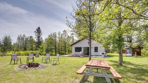 En trädgård med ett picknickbord, fyra stolar, en eldstad och en liten stuga.