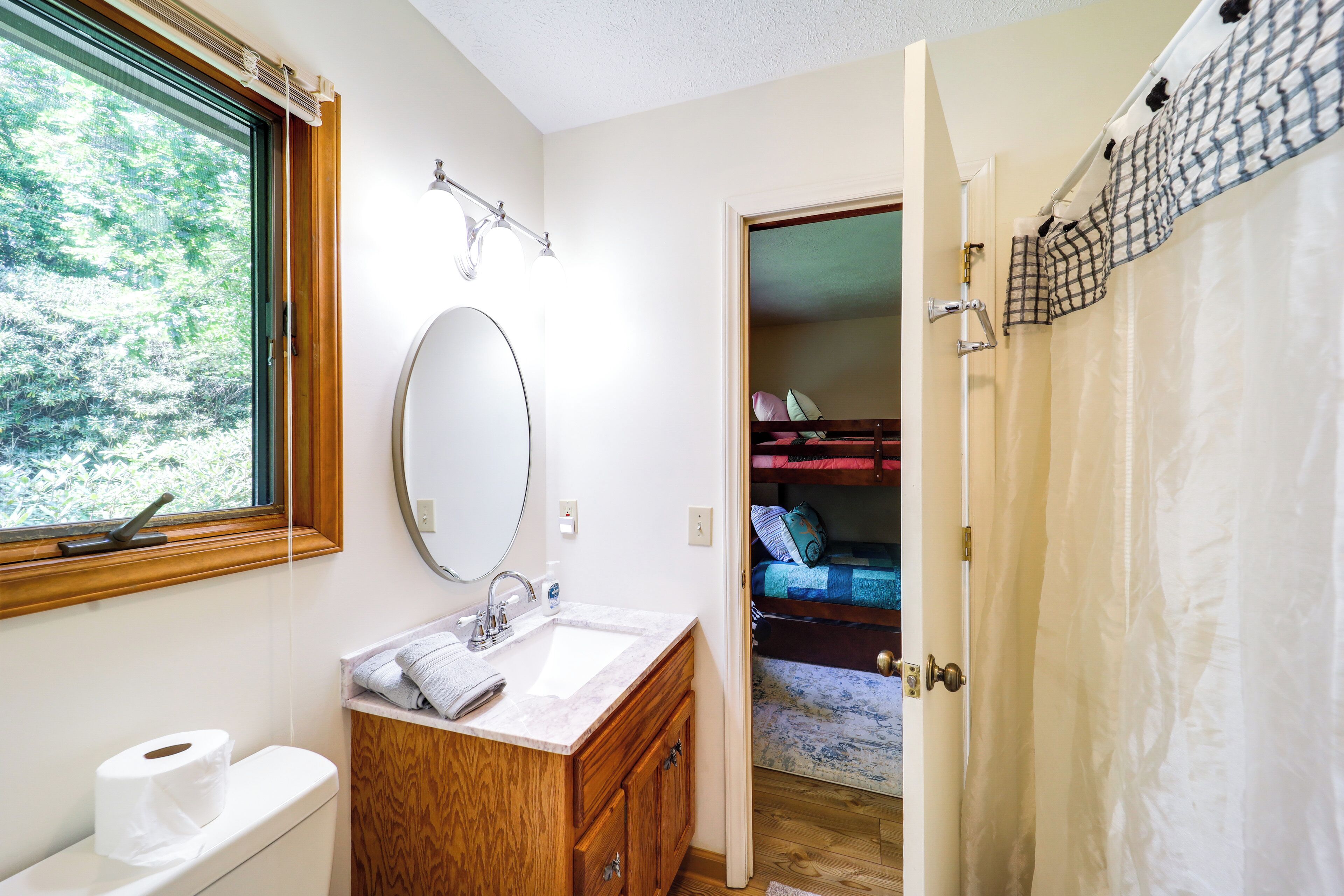 Ein Badezimmer mit Toilette, Waschbecken und Spiegel. Ein Fenster bietet Blick auf Bäume.