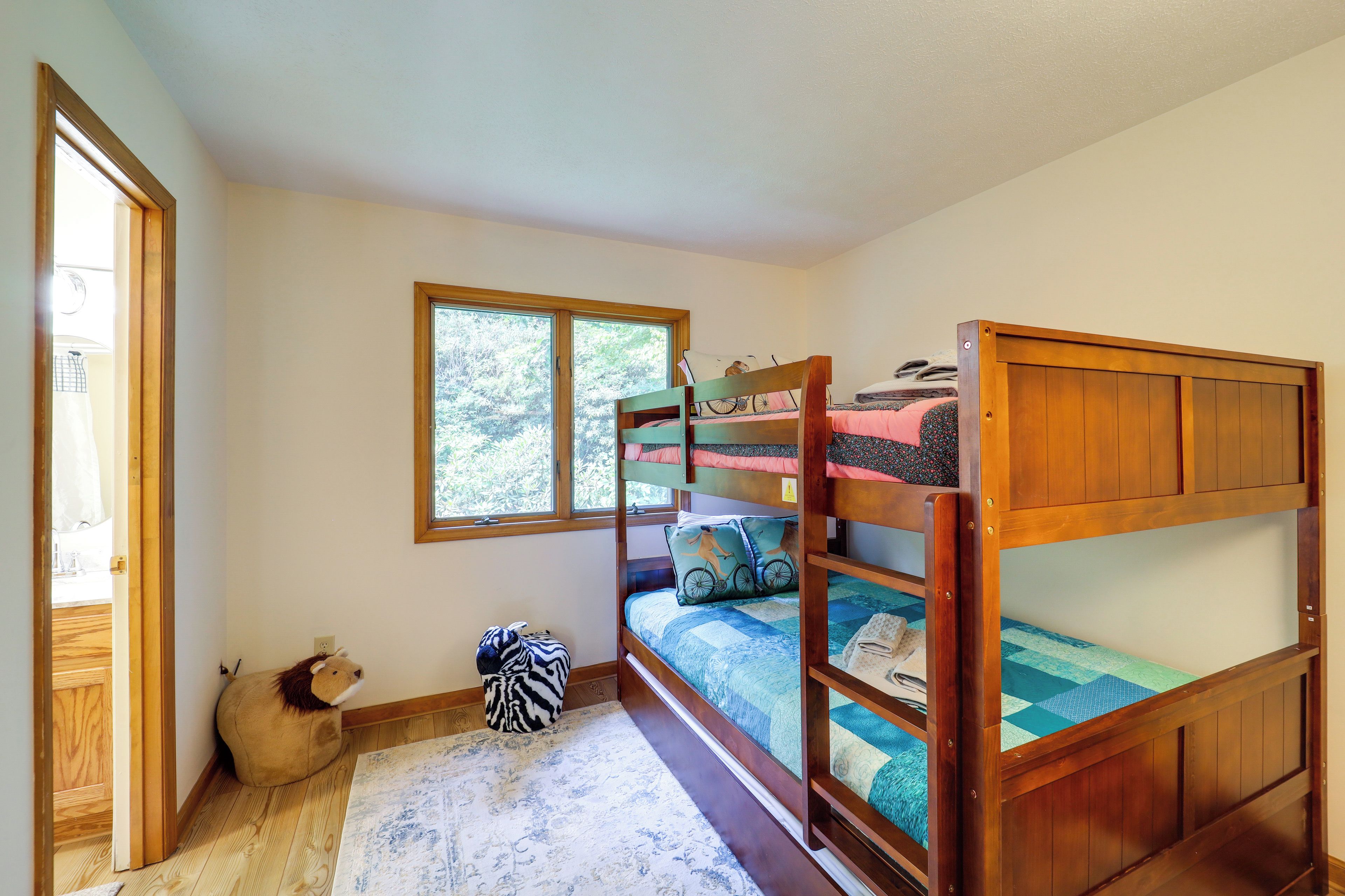 Quarto com cama de solteiro e beliche, janela, tapete e um bicho de pelúcia.