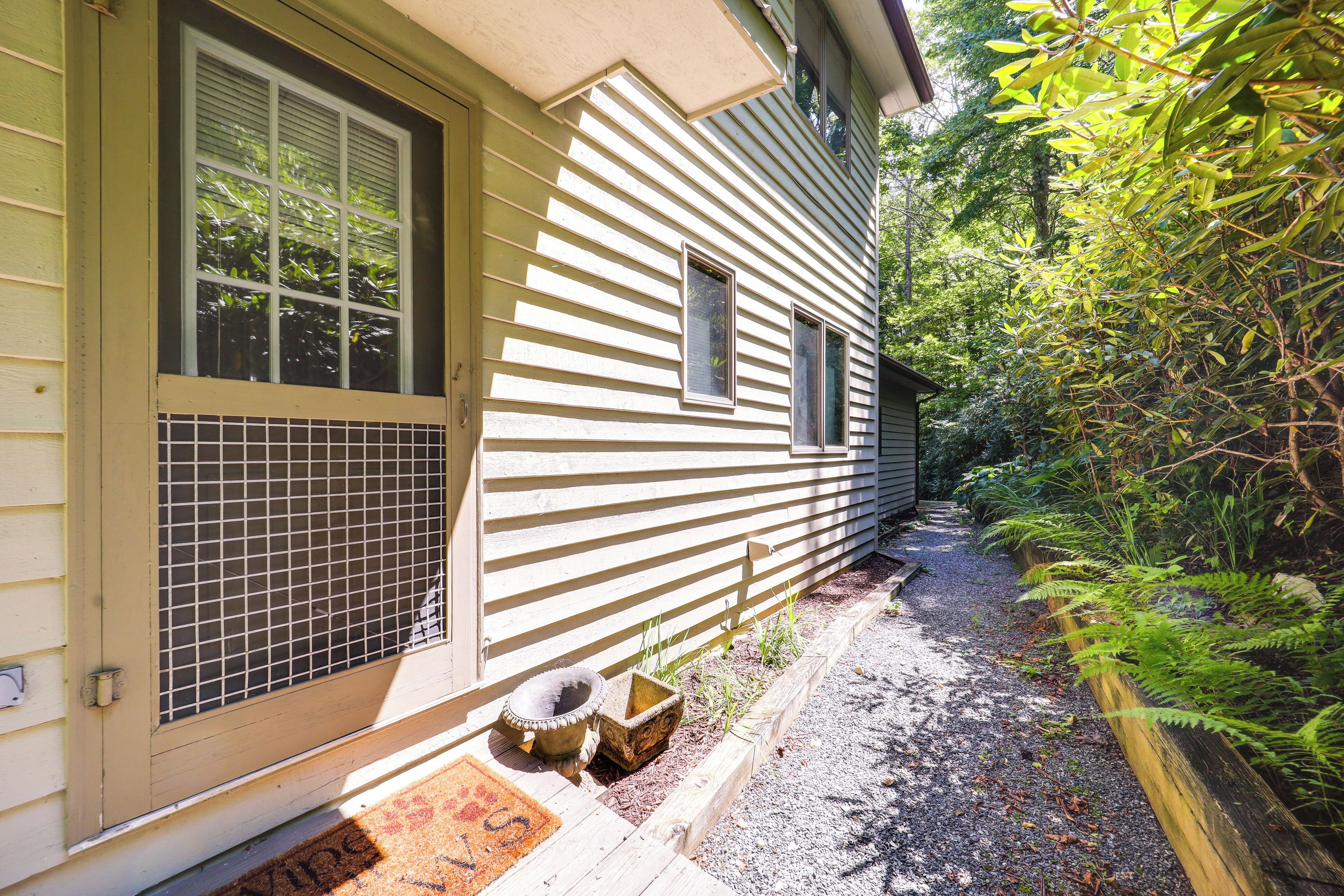A house with a front porch, a small garden area with a wooden planter, and a gravel path leading to the door.