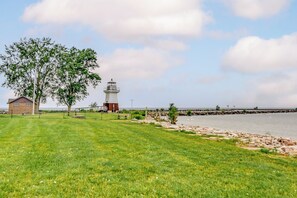 A grassy area with a lighthouse, a small building, and a rocky shoreline by the water. - Point Breeze Vacation Rental, Walk to Lake Ontario (Kent)